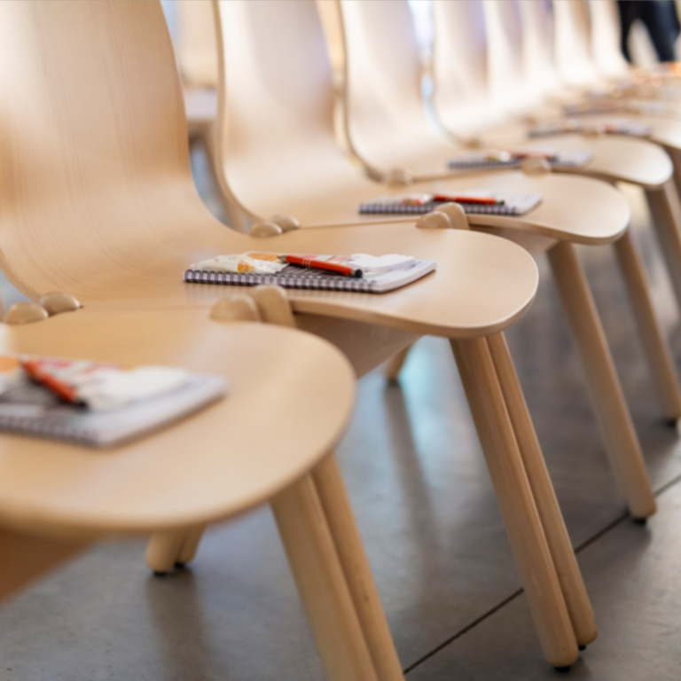 A row of empty chairs with a notepad and a pen.
