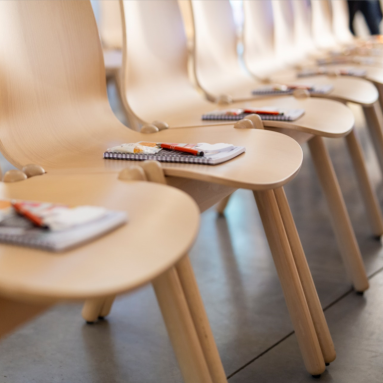 Een reeks lege stoelen met een blocnote en een pen.