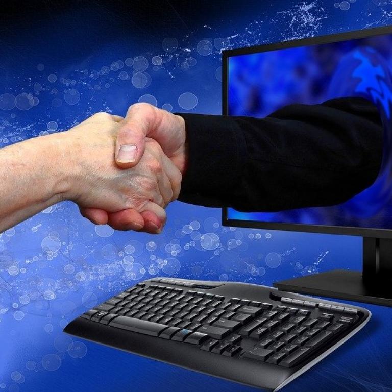 Handen die elkaar schudden door een computerscherm